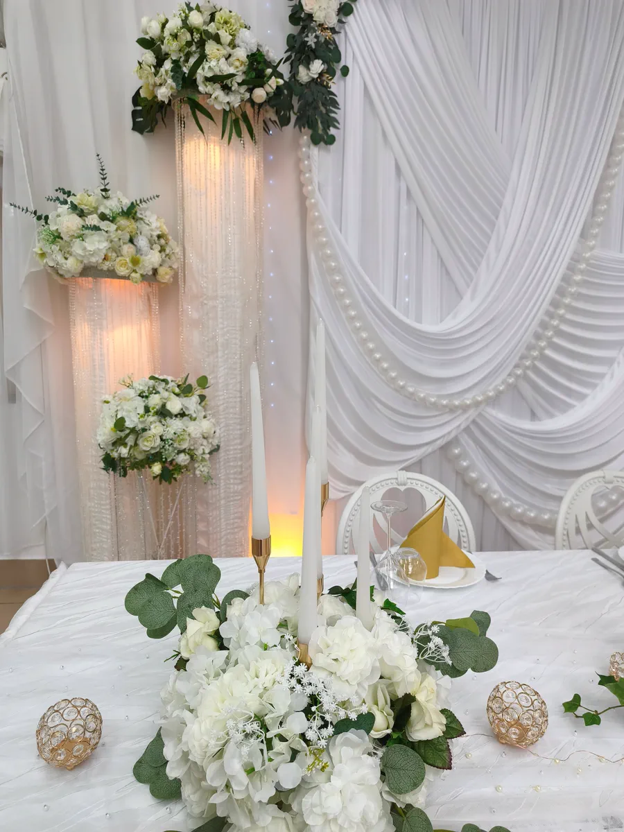 Dekoration mit weißen Blumengestecken, Perlenvorhang, Kerzen und beleuchteten Säulen