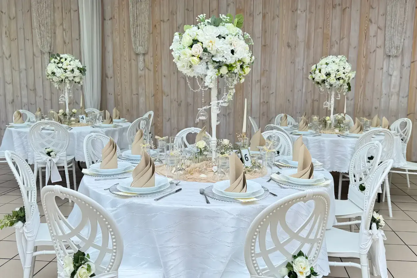 Runde Tafeln mit weißen Louis-Stühlen und hohen Blumengestecken
